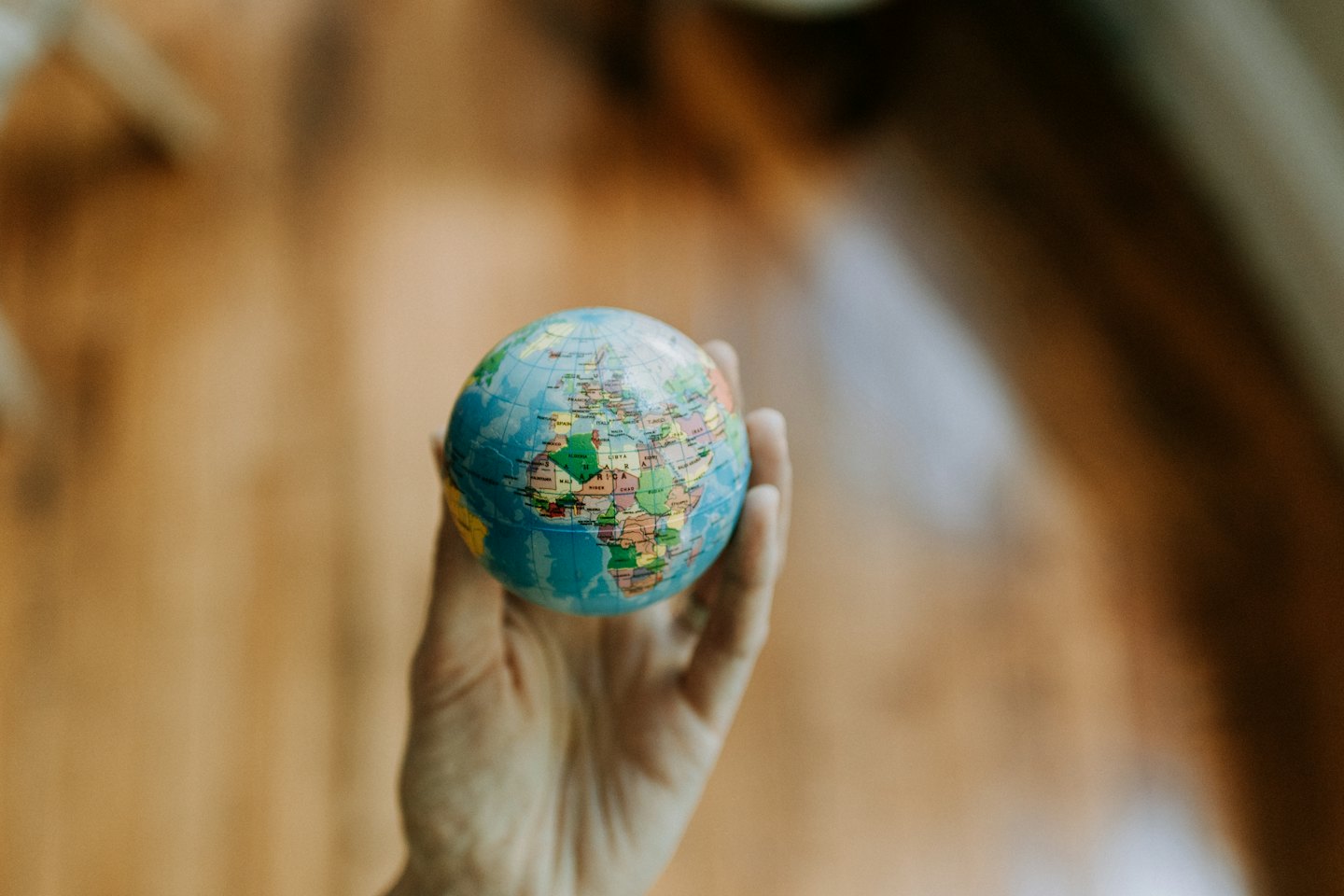 Een hand die een kleurrijke wereldbol met blauwe oceanen vasthoudt.